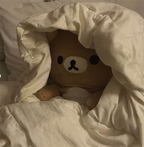 A Brown Teddy Bear Sitting Under A Blanket On Top Of A White Comforter
