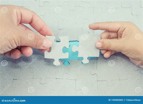 Two Hands Trying To Connect Two Puzzle Pieces On Blue Wooden Puzzle