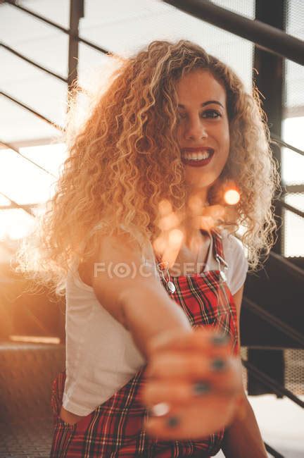 Smiling Young Curly Woman Showing Blurred Sparkler On Stairs In