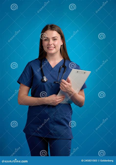 Smiling Nurse Standing And Holding Clipboard By Her Hands Looking
