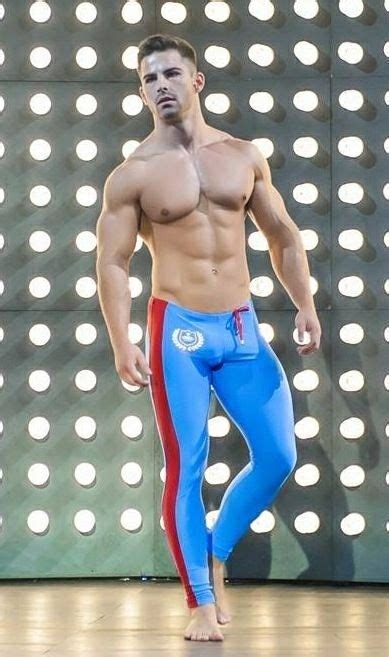 A Shirtless Man In Blue And Red Pants Standing On A Stage With Lights Behind Him