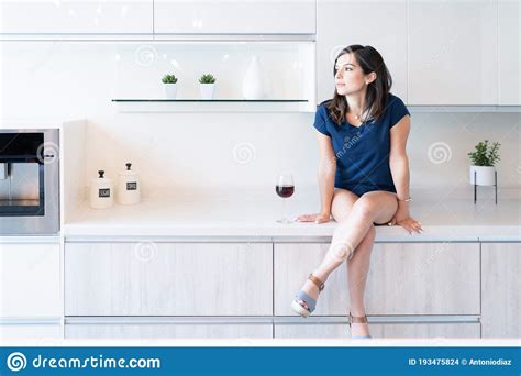 Thoughtful Woman Sitting On Countertop In Kitchen Stock Photo Image