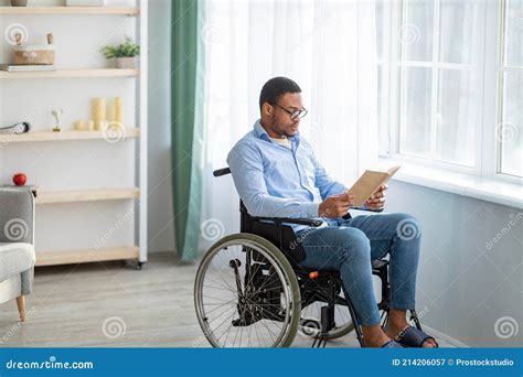 Millennial Handicapped Black Man In Wheelchair Eating Breakfast And Reading Book Indoors Royalty