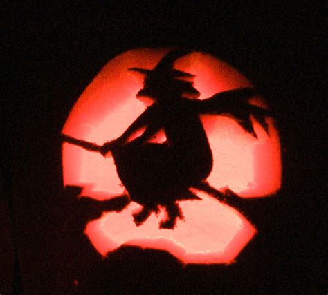 A Carved Pumpkin With A Silhouette Of A Witch On It