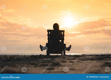 Girl Is Sitting On The Sun Lounger On The Beach At Sunset Stock Photo