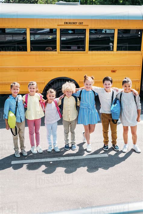 Group Of Happy Schoolchildren Standing In Front Of School Bus And