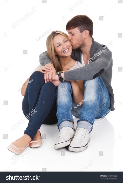 Young Couple In Love Sitting Close Together On The Floor In An Affectionate Embrace Smiling At