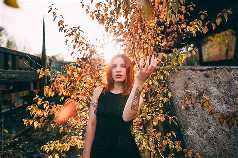 Ginger Woman Posing With A Yellow Bush Behind At Sunset By Stocksy Contributor Thais Ramos