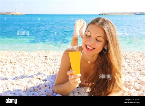happy smiling woman holding sun cream tube protection lying on pebbles beach sunscreen girl