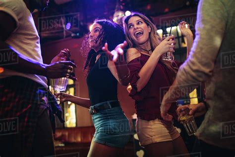 Happy Young Women Dancing And Partying With Male Friends At Nightclub
