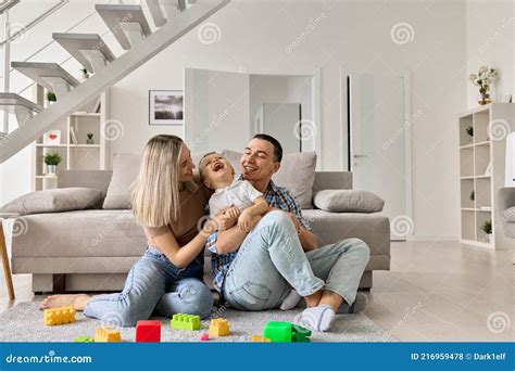 Happy Young Adult Parents With Child Sitting On Floor In Modern Living