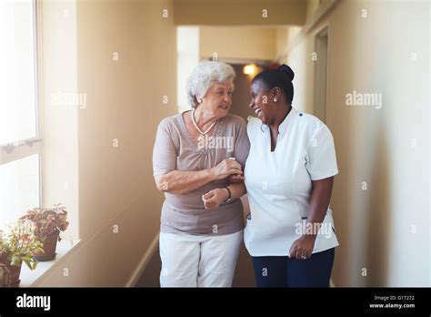 Portrait Of Happy Female Caregiver And Senior Woman Walking Together At