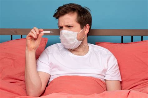 Sick Man Lying On Bed Checking His Temperature At Home Stock Photo