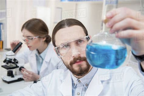 Pensive male scientist holding flask with chemical reagent ...