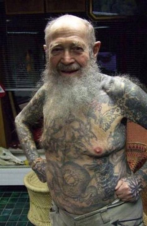 an older man with tattoos on his body and chest standing in front of a chair