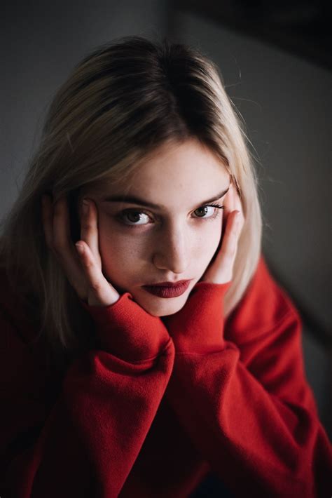 A Woman With Her Hand On Her Face Looking At The Camera While Wearing A Red Sweater