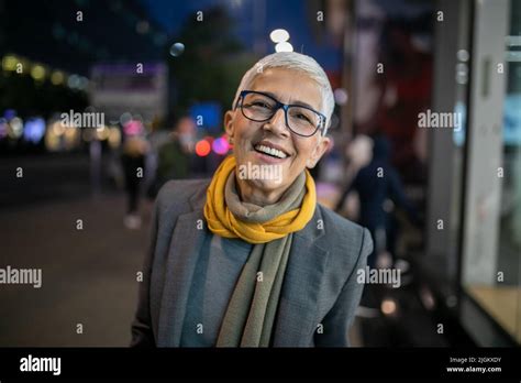 Smiling Mature Senior Woman With Short Gray Hair And Eyeglasses Walking On Street City Night