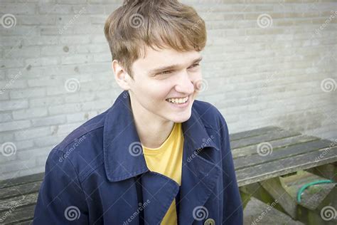 Handsome Young Man Sitting On A Bench Smiling Candid Stock Photo