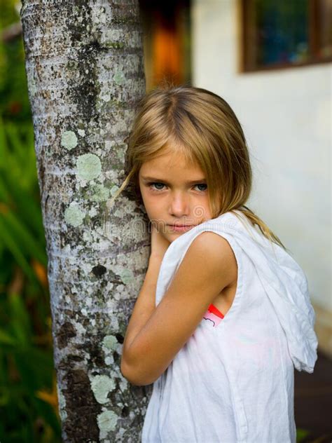 Charming Little Girl Standing Near The Tree Wearing White Dress And
