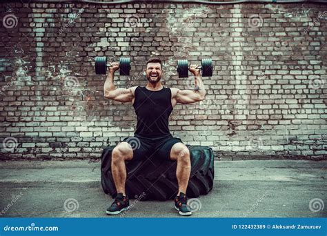 Muscular Guy Doing Exercises With Dumbbell Against A Brick Wall Stock