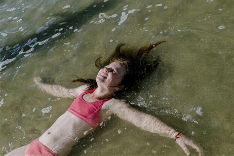 Girl Lying Down In Water At Beach On Sunny Day Stock Photo