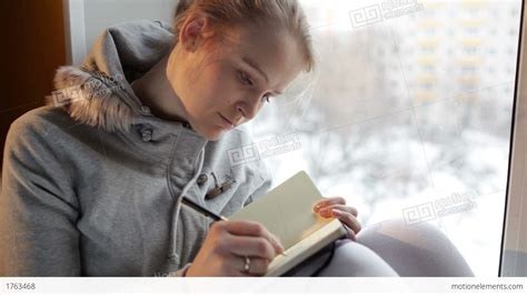 Young Girl Writing In Her Journal While Sitting At A Large Window Stock