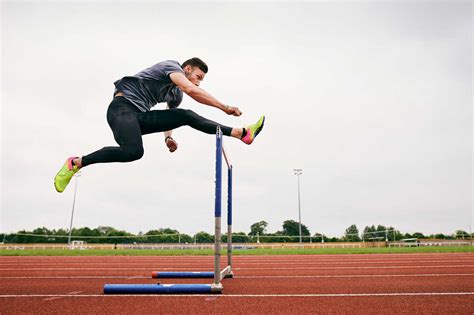 Athlete Jumping Over Hurdle On Running Track Stock Photo