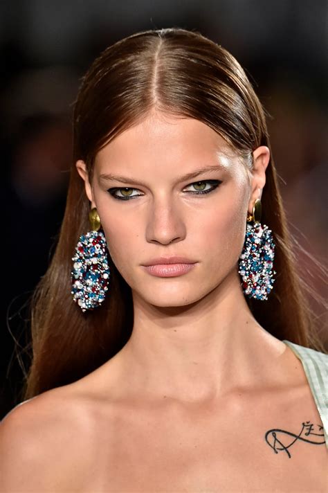 a model with long hair and earrings on the runway