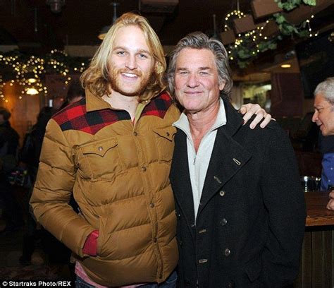 Two Men Standing Next To Each Other In Front Of A Christmas Tree With Lights Hanging From The