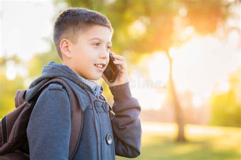 Young Hispanic Boy Walking Outdoors With Backpack Talking On Cell Phone