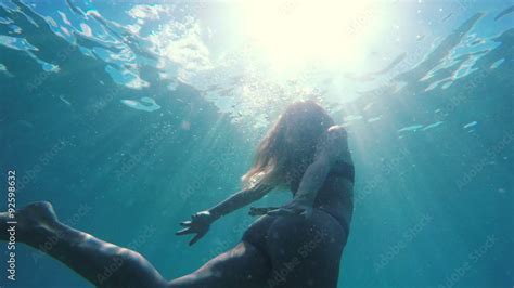 Woman In Bikini Swimming Underwater Towards Surface With Beautiful Sun Flares In Slow Motion