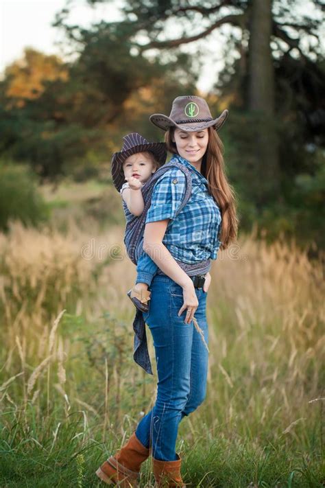 Cowgirl Mother Carrying Her Small Daughter In A Baby Sling Stock Photo