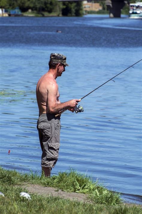 Fisherman Stands On The River Bank And Holds A Fishing Pole Editorial