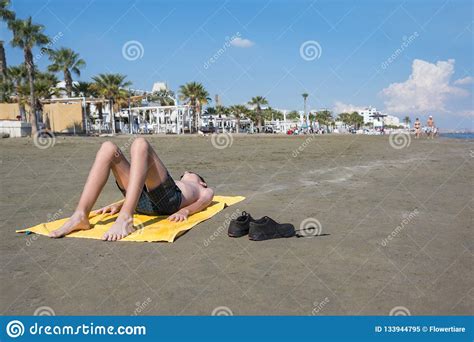 Teen Boy Lies On Yellow Towel And Sunbathes On The Beach Traveling On