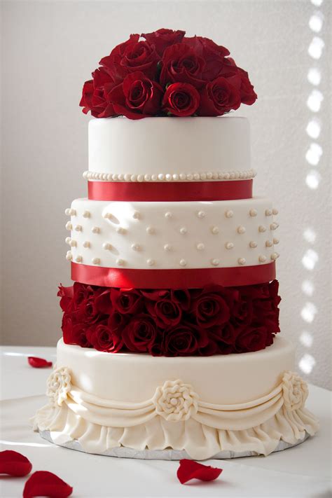 A Three Tiered Wedding Cake With Red Roses On Top