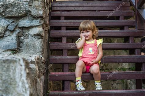 Charming Little Girl Baby Sitting On The Wooden Stairs In A Beautiful