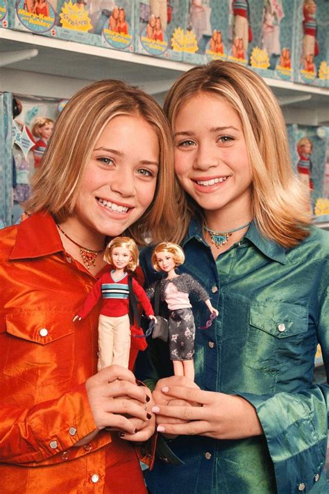 Two Young Women Standing Next To Each Other With Dolls In Front Of Them And Smiling At The Camera