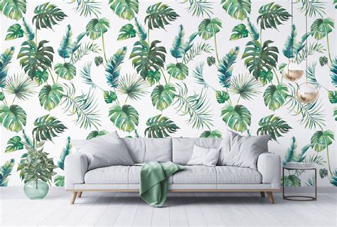 A White Couch Sitting In Front Of A Wall With Green Palm Leaves Painted