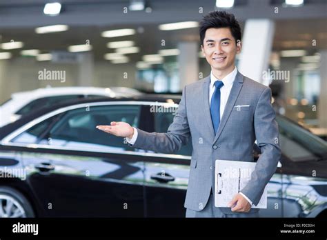 Confident salesman standing with new car in showroom Stock Photo - Alamy