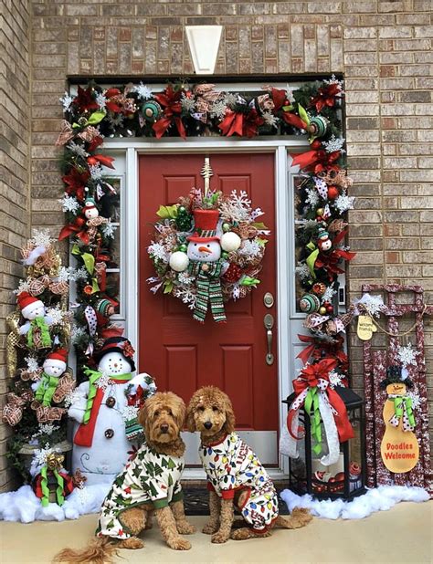 Two Dogs Sitting In Front Of A Red Door Decorated With Christmas