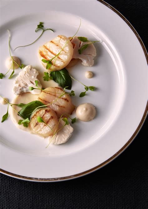 A White Plate Topped With Scallops And Greens
