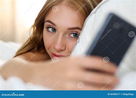 Young Beautiful Blonde Woman Lying In Bed Holding Cellphone Stock Image
