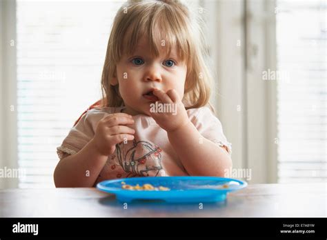 Baby Girl Eating Food While Looking Away At Home Stock Photo Alamy