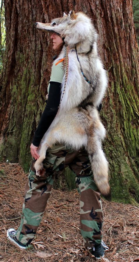A Man In Camo Pants Holding A Wolf On His Back While Standing Next To A