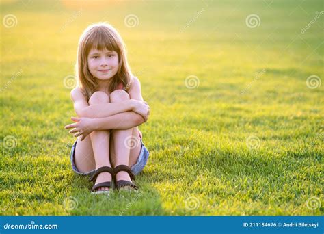 Young Pretty Child Girl Sitting On Fresh Green Grass Lawn On Warm