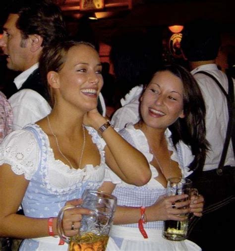 Two Women Dressed In Traditional Bavarian Clothing Holding Wine Glasses And Smiling At The