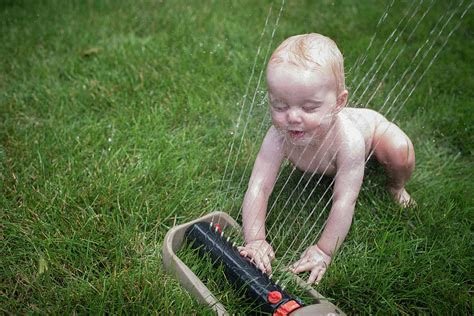 High Angle View Of Naked Baby Boy Playing With Sprinkler On Grassy