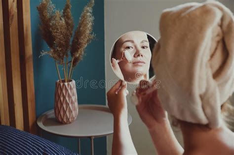 Close Up Mirror Woman Using Jade Facial Roller For Face Massage Sitting On Bed In Bedroom