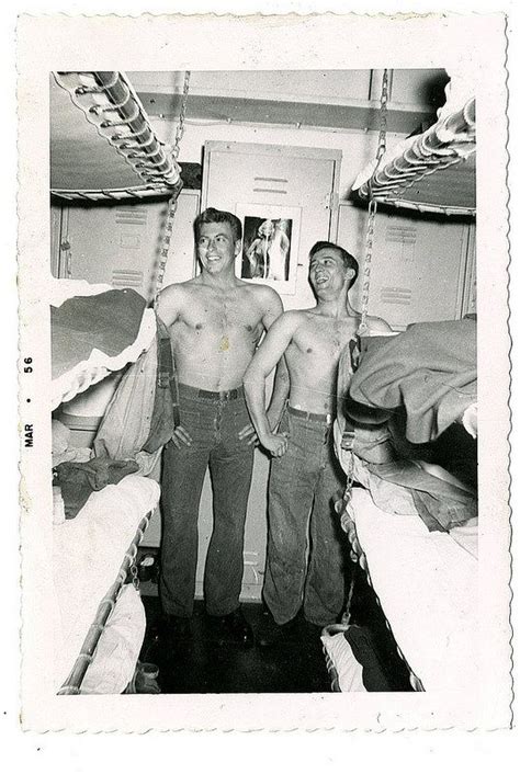 Two Men Standing Next To Each Other In A Room With Bunk Beds And Mattresses