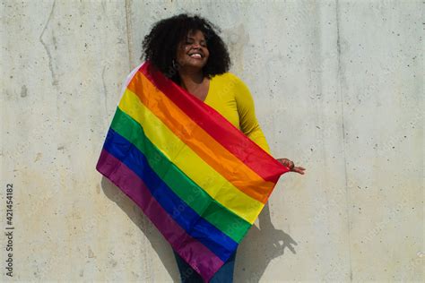 very happy african american lesbian woman with the gay pride flag on her body on a grey